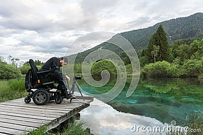 Man on wheelchair using mirrorless camera near the lake in nature Stock Photo