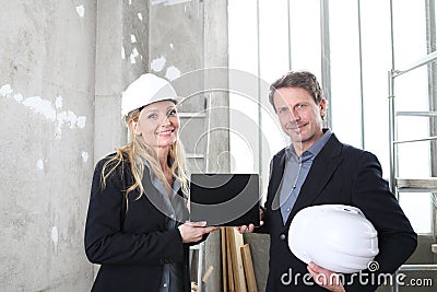 Smiling man and woman architects or engineers show the screen of the digital tablet work together in the inside the construction Stock Photo