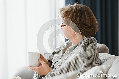 Smiling mature elder 65s woman sitting relaxing with cup of tea, coffee. Senior mid age stylish look woman with Stock Photo