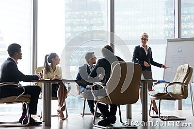 Smiling mature female coach making flipchart presentation to wor Stock Photo