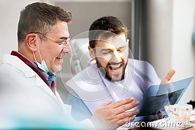 Mature male dentist and young patient looking at teeth x-ray image after successful medical intervention Stock Photo