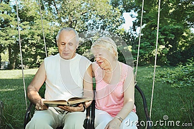 Smiling mature man and woman 65-69 years old reading a book in Stock Photo