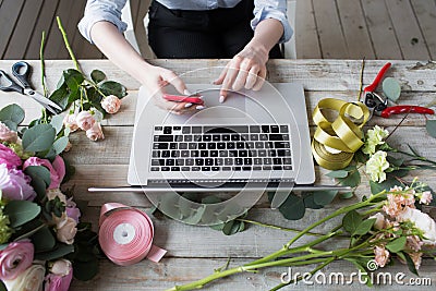 Smiling Mature Woman Florist Small Business Flower Shop Owner. She is using her telephone and laptop to take orders for Stock Photo