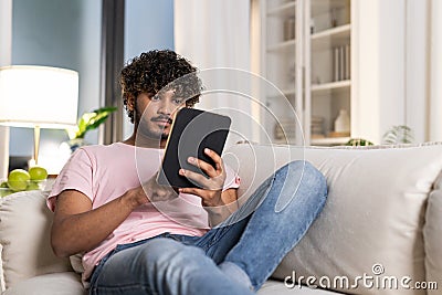 A smiling mestizo guy reclining on the sofa in the room, enjoys relax after work or study in the cozy home environment Stock Photo