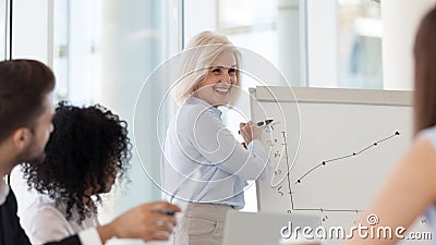 Smiling middle-aged female coach presenting business plan on flipchart Stock Photo