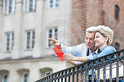 Smiling middle-aged man showing something to woman with guidebook in city Stock Photo