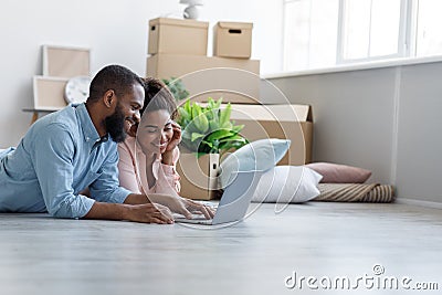 Smiling millennial african american male and female lies on floor in new apartment among boxes, planning interior Stock Photo