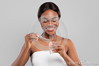 Smiling millennial black lady take care of face and use cosmetic serum oil, making facial massage Stock Photo