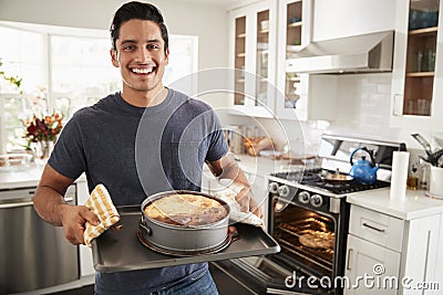 Smiling millennial Hispanic man standing in kitchen presenting the cake he has baked to camera Stock Photo