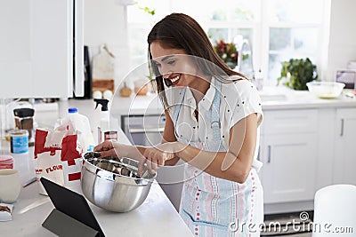 Smiling millennial woman preparing cake mixture, following a recipe on a tablet computer Stock Photo