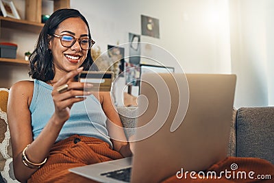 Smiling mixed race woman using credit card for ecommerce on laptop at home. Happy hispanic sitting alone on living room Stock Photo