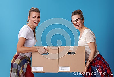 Smiling modern female roommates with cardboard boxes on blue Stock Photo