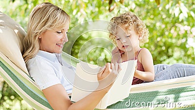 Smiling mom reading a story from the book to the little girl daughter child blue eyes with blond curly hair, together lying on the Stock Photo