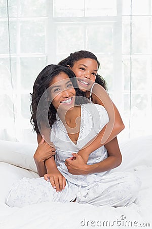 Smiling mother and daughter posing together on bed Stock Photo