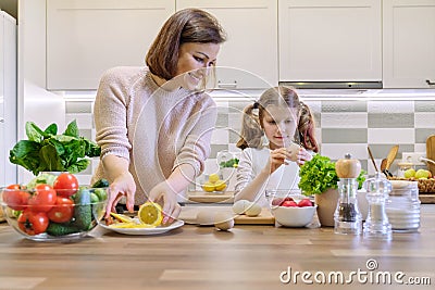 Smiling mother and daughter 8, 9 years old cooking together in kitchen vegetable salad. Healthy home food, communication parent Stock Photo