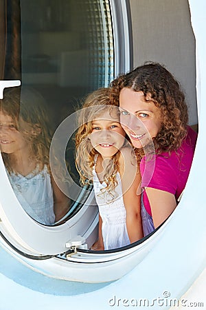 Smiling mother and her daughter look out from window Stock Photo