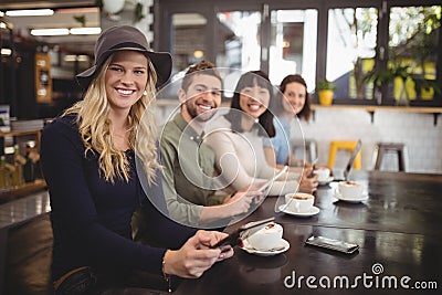 Smiling multi ethnic friends sitting with coffee cups and mobile phones at table Stock Photo