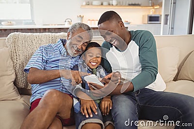 Smiling multi-generation family using mobile phone in living room Stock Photo