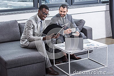 smiling multiethnic businessmen sitting on couch and having discussion Stock Photo