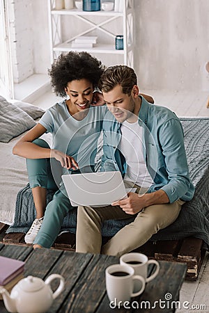Smiling multiracial couple looking at laptop screen while sitting Stock Photo