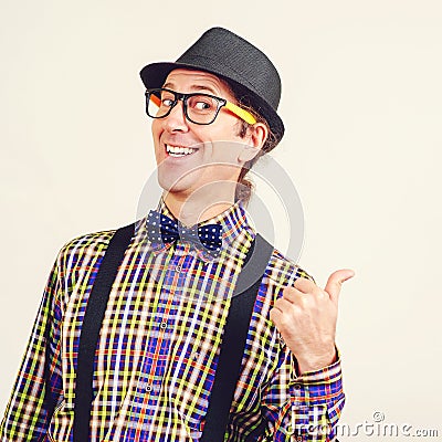 Smiling nerd man in bow tie and suspenders is showing thumbs up. Happy geeky hipster wears retro hat and clothes. Gesturing OK Stock Photo