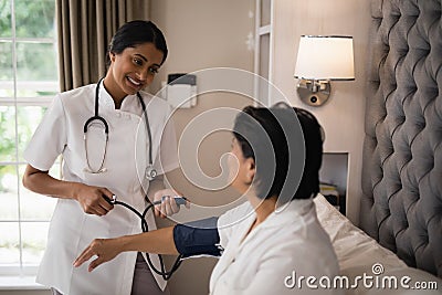 Smiling nurse checking blood pressure of patient resting on bed Stock Photo