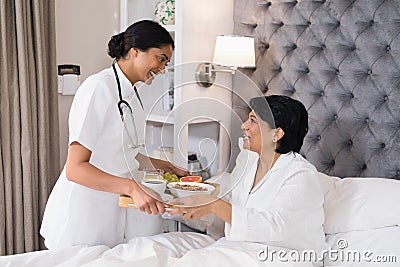 Smiling nurse serving breakfast to patient resting on bed Stock Photo