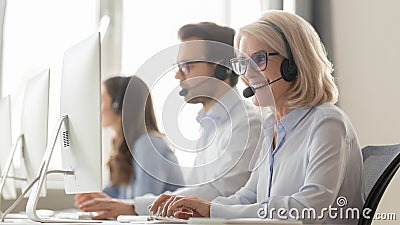 Smiling old female call center agent in headset consulting client Stock Photo