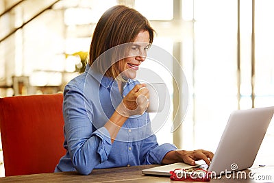 Smiling older woman drinking coffee and looking at laptop Stock Photo