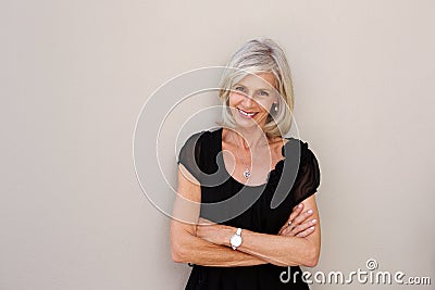 Smiling older woman leaning on wall with arms crossed Stock Photo