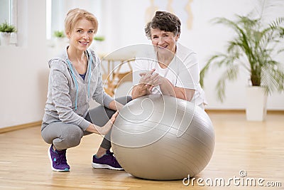 Smiling physiotherapist with elderly woman laying on exercising ball during physical therapy Stock Photo