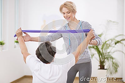 Smiling physiotherapist helping senior woman working out with resistance bands Stock Photo