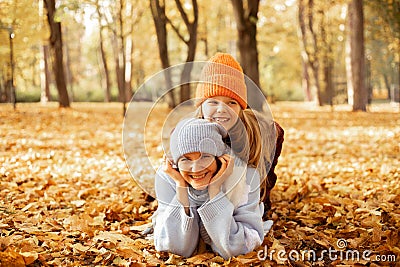 Smiling pleased relaxed mischief mother and daughter look camera, wear warm hats and coats, have fun in autumn woodlands Stock Photo