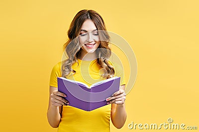 Smiling positive girl reading book on yellow background Stock Photo