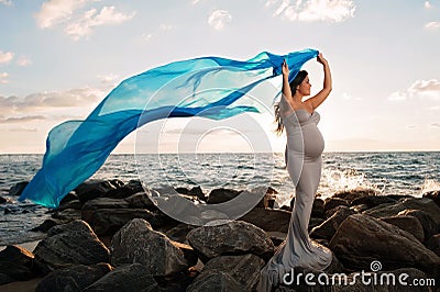 Smiling Pregnant Woman on the Beach with Blue Veil Stock Photo