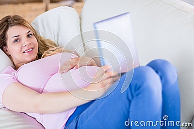 Smiling pregnant woman looking at camera and using tablet Stock Photo