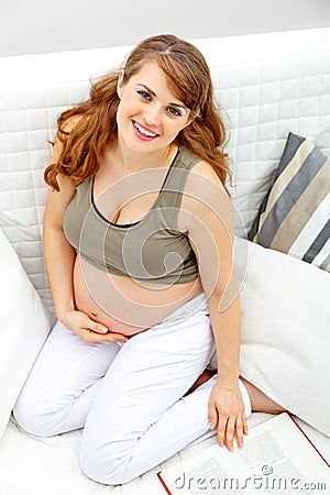 Smiling pregnant woman sitting on sofa with book Stock Photo