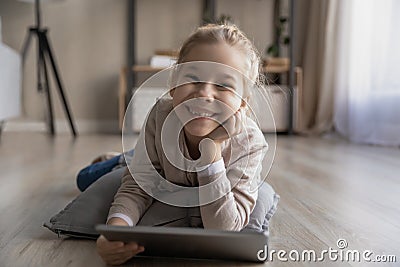 Smiling preteen girl lying on warm floor holding digital tablet Stock Photo