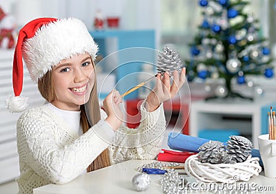 Smiling preteen girl in Santa hat preparing for Christmas paintig pine cone Stock Photo