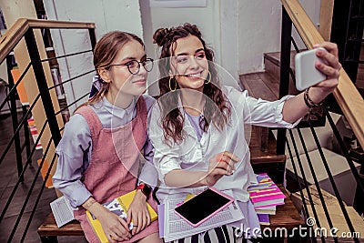 Smiling pretty ladies making selfie with smartphone while sitting Stock Photo