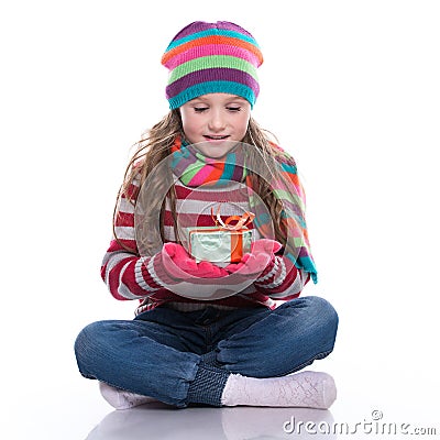 Smiling pretty little girl wearing coloful knitted scarf, hat and gloves, holding christmas gift isolated on white background. Win Stock Photo