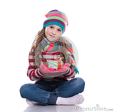 Smiling pretty little girl wearing coloful knitted scarf, hat and gloves, holding christmas gift isolated on white background. Stock Photo