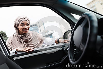 Smiling pretty muslim african american woman buyer in hijab looks into salon of new car, customer choose transport Stock Photo