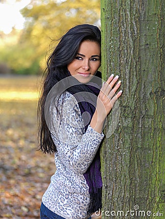 Smiling Pretty Young Woman Leaning on Tree Trunk Stock Photo