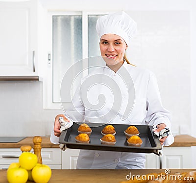 Proffesional woman cook in white uniform holding sheet pan with just baked cupcakes Stock Photo