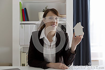 Smiling real estate saleswoman holding white model house. Real e Stock Photo