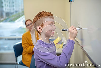 Smiling red-haired boy writing symbols on the whiteboard Stock Photo