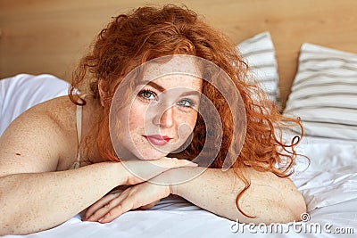 Smiling red haired female enjoy weekends lying on bed Stock Photo