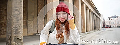 Smiling redhead european girl drives public e-scooter, tourist explores city, rides in city centre Stock Photo