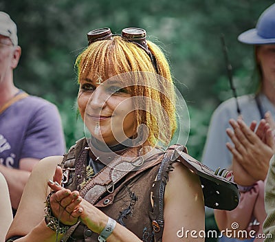 Smiling redhead young woman in leather costume claps hands at public fantasy festival Editorial Stock Photo